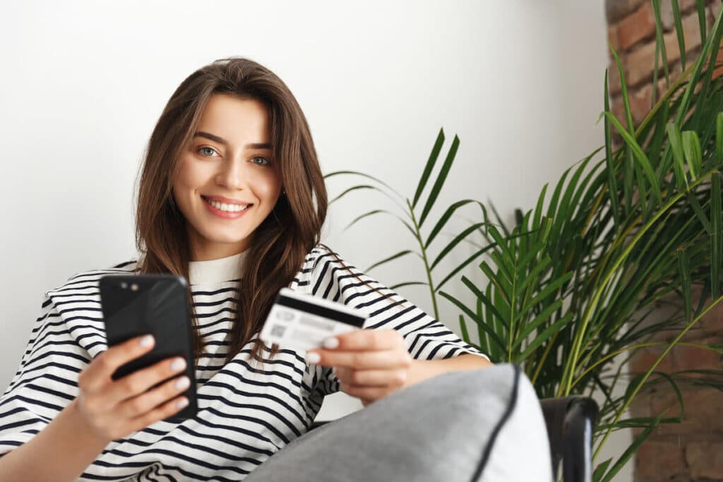 Woman smiling at the camera while holding a phone and a credit card
