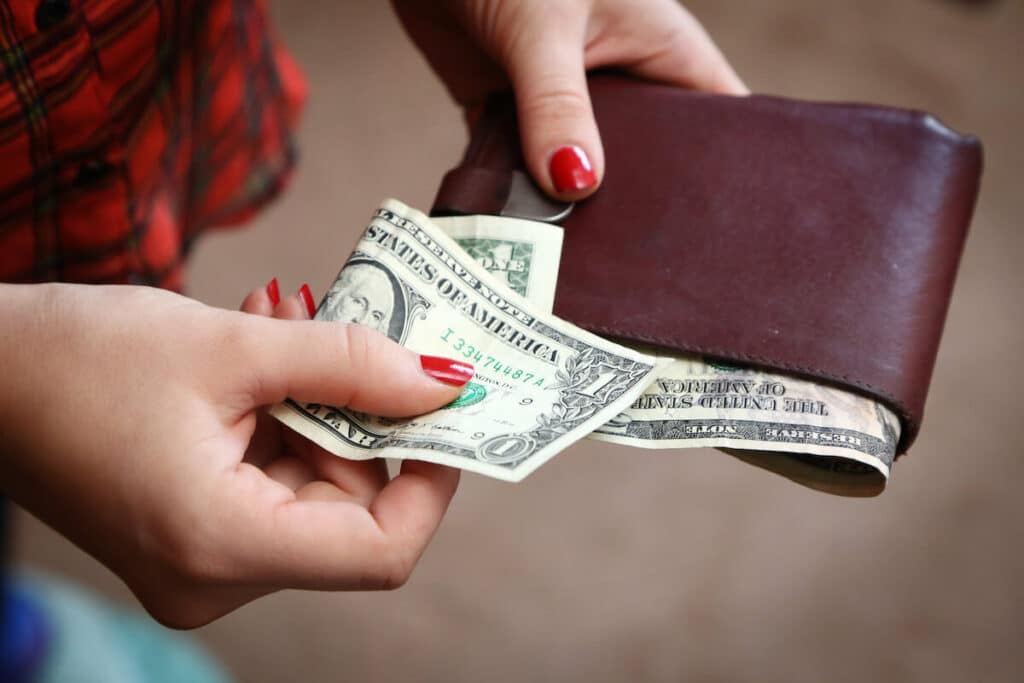 Person pulling out a US dollar bill from a wallet