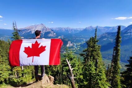 finance tips when moving to canada will prepare you like this man with a canadian flag on a mountain