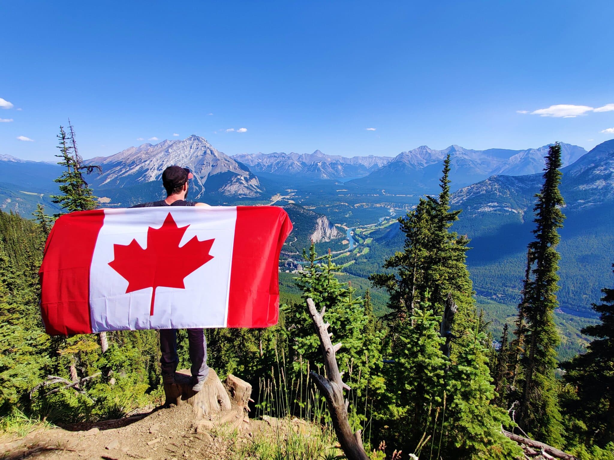 finance tips when moving to canada will prepare you like this man with a canadian flag on a mountain