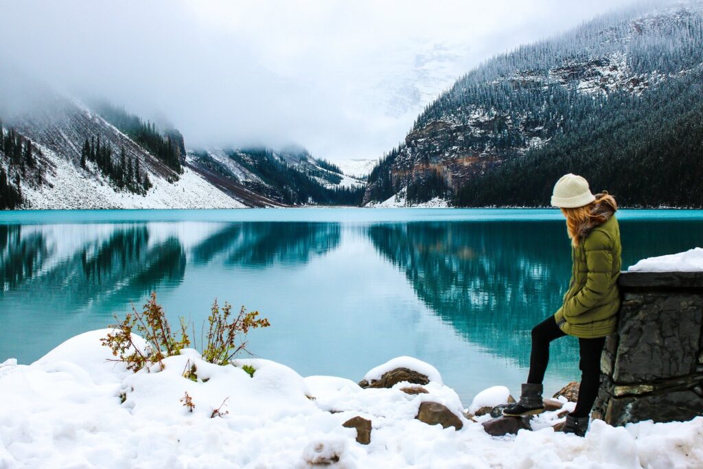 Une femme devant un lac, contemplant le paysage montagneux enneigé