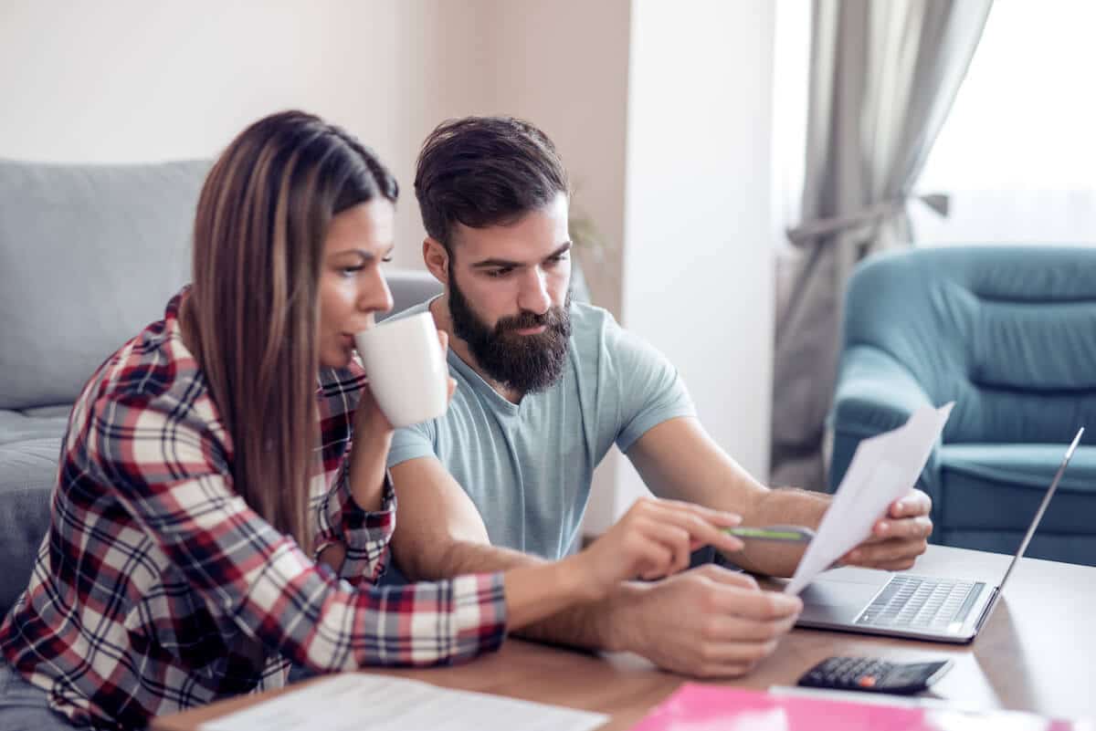 Una pareja leyendo un documento frente a una computadora y una calculadora