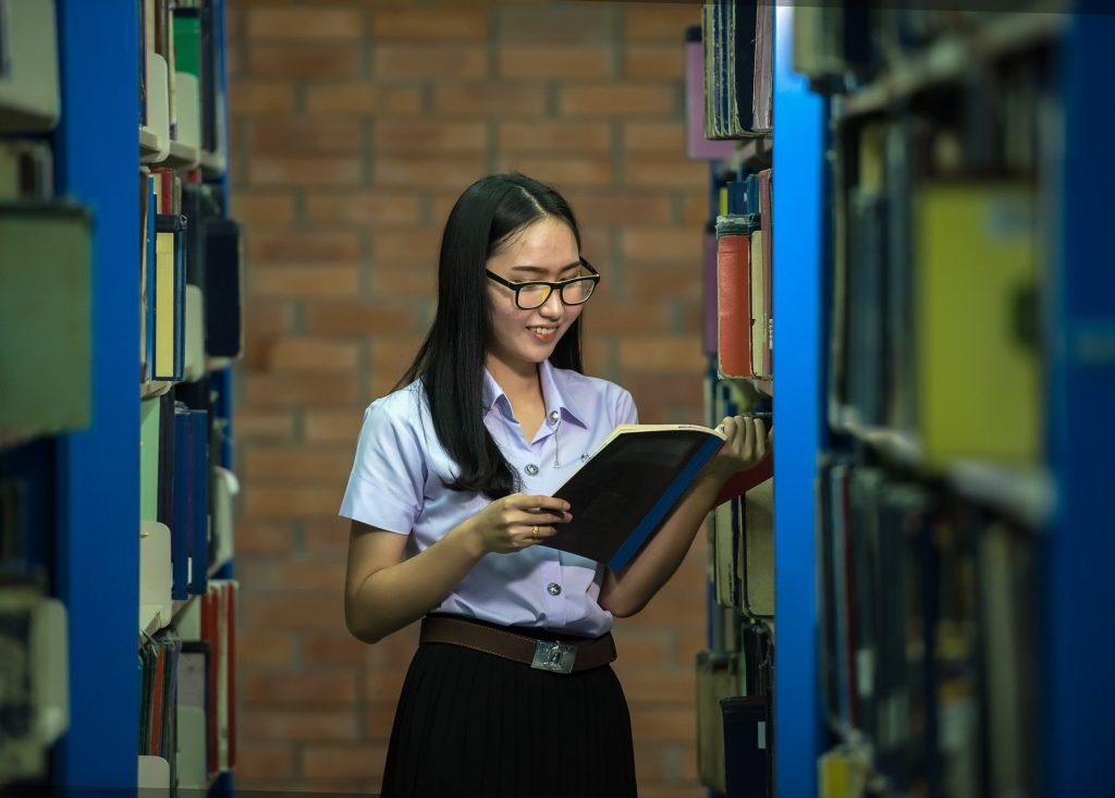 Una estudiante sosteniendo un libro en una biblioteca.