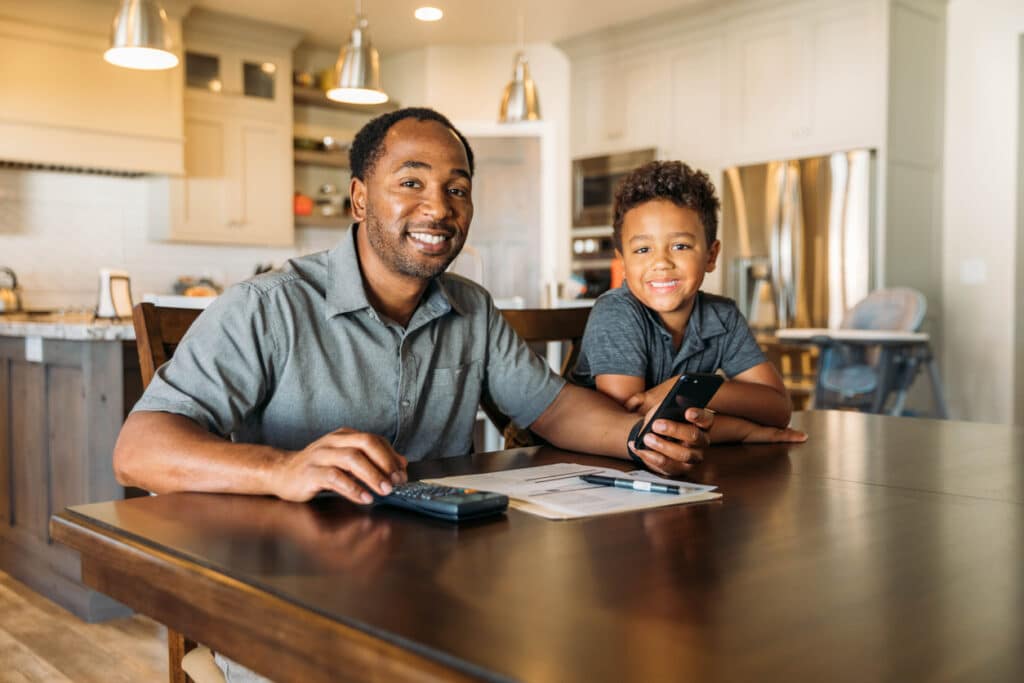 smiling African father using a budget app to teach his son about finances
