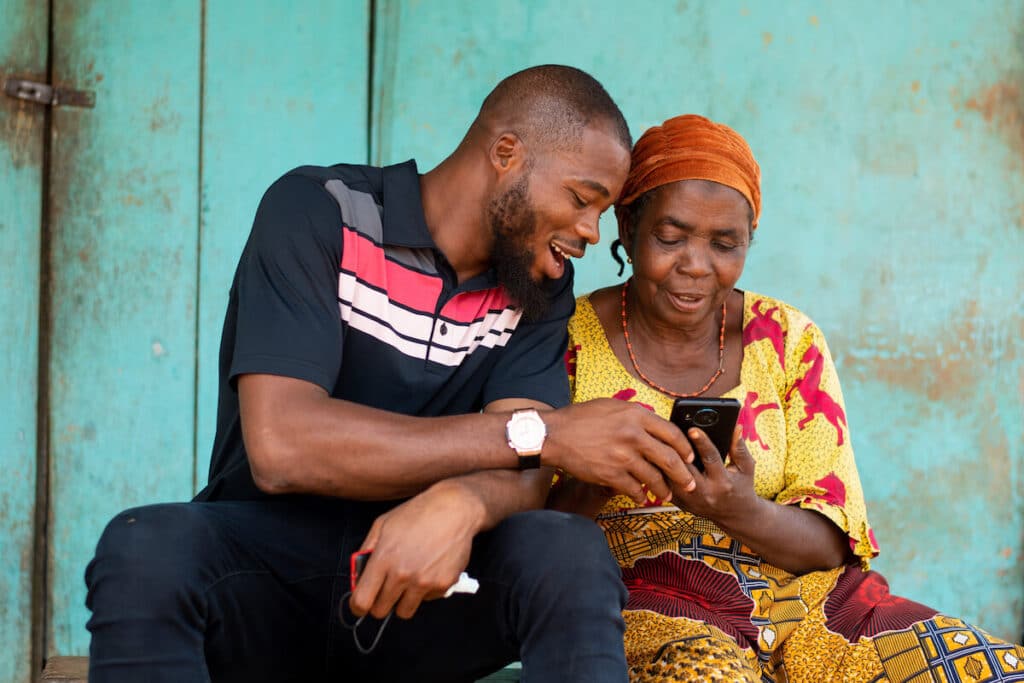 Gambia currency: man teaching an older woman how to use a smartphone
