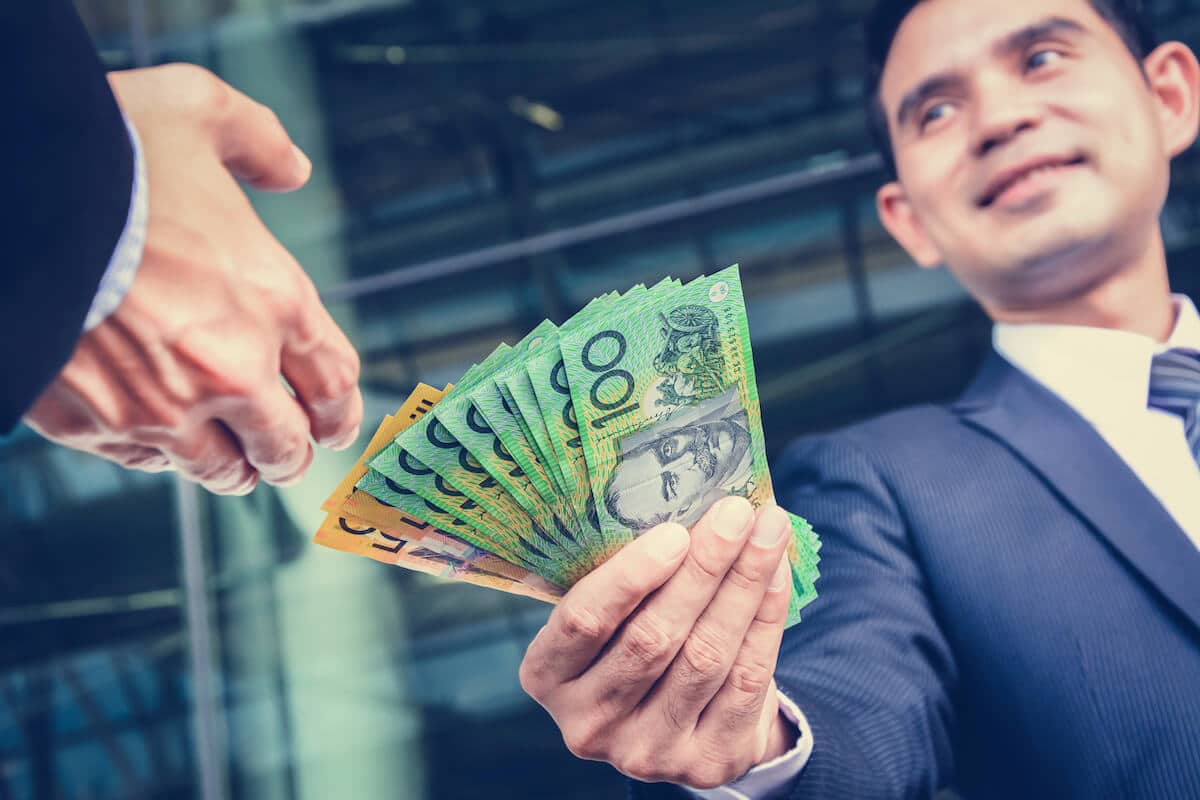 Une personne souriante donnant une somme en dollars australiens en espèces à une autre personne