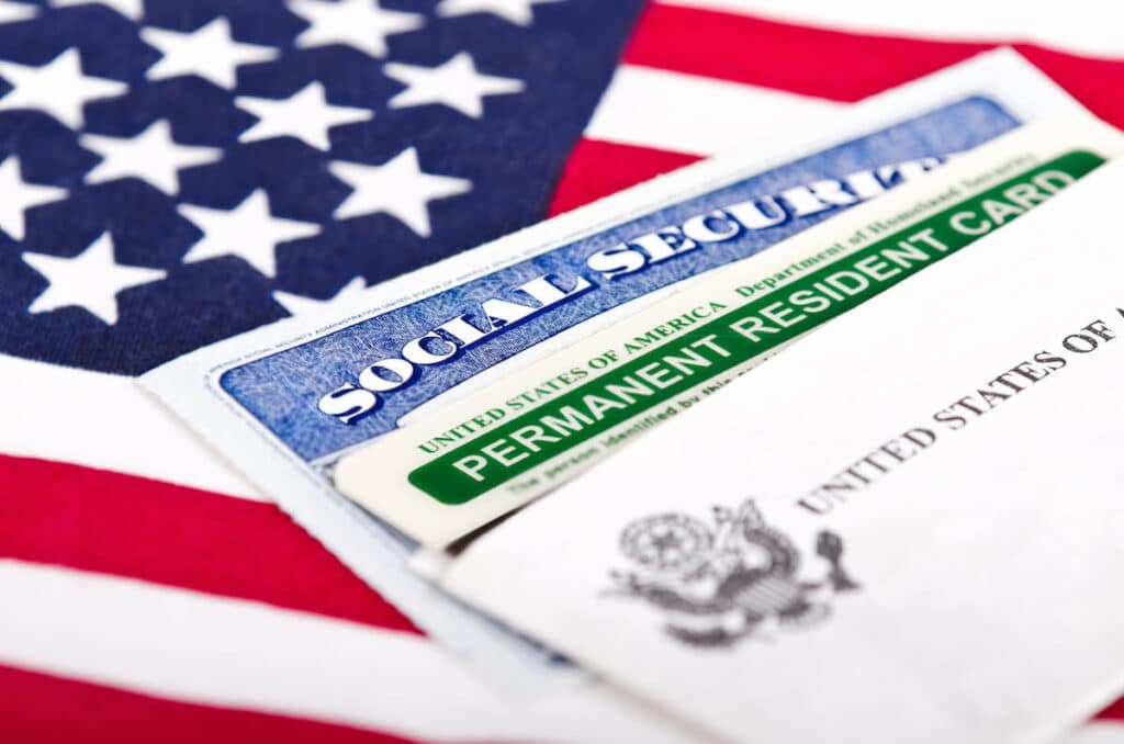 Una tarjeta verde y una tarjeta de seguridad social colocadas en la bandera de los Estados Unidos.