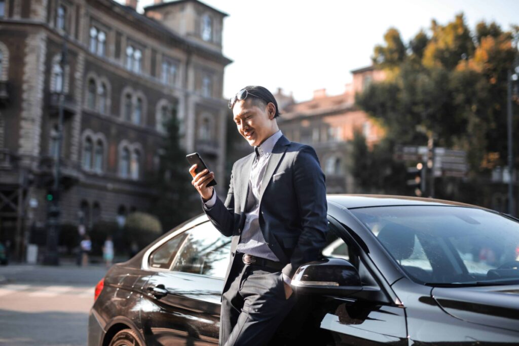 Geld nach Hause schicken: Mann lehnt an einem Auto und sieht auf sein Handy