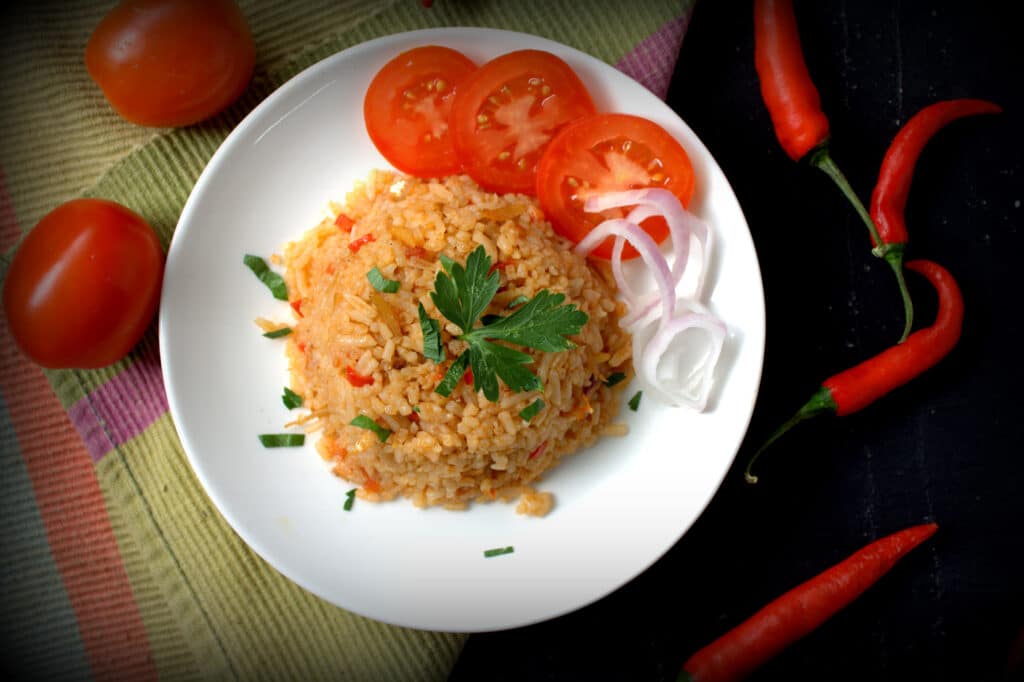jollof rice in a plate with slices of tomatoes