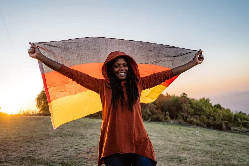 Junge afrikanische Frau hält auf einer Wiese eine deutsche Flagge als Repräsentation von Einwanderern in Deutschland, die Überweisungen senden.
