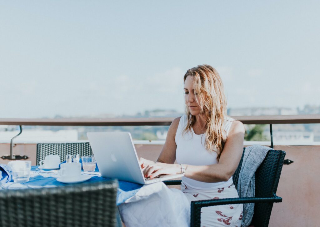 Una mujer trabajando en su computadora portátil bajo el sol en una terraza