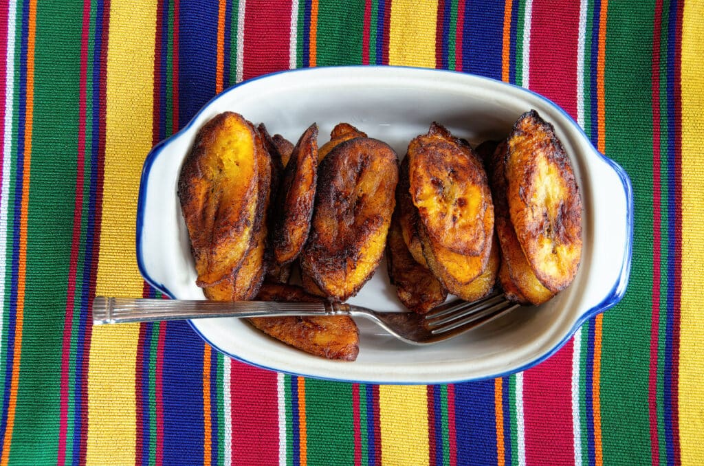 Jamaican food includes fried plantains like these on a colorful table array.