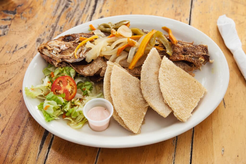 Escovitch fish, served here on a white plate with bread and salad, is a traditional Jamaican dish.