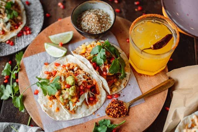 Two tacos on a cutting board with a cocktail