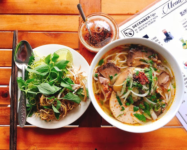 Bowl of pho with chili sauce and herbs and toppings