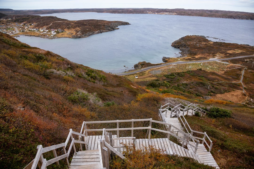 A picture of Dare Devil Trail, St. Anthony, Newfoundland, Canada showing wooden stairs going up a rocky cliff on the Atlantic Ocean Coast during a cloudy day