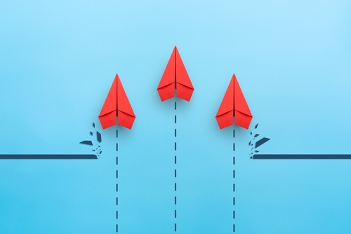 Three red paper airplanes breaking through a barrier